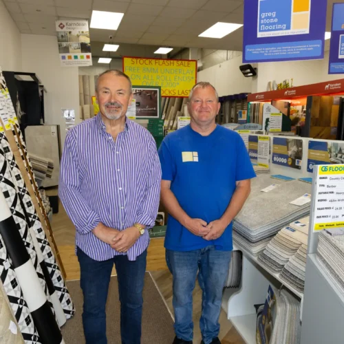 Two Greg Stone Flooring team members standing inside the showroom, with carpet samples and flooring displays around them.